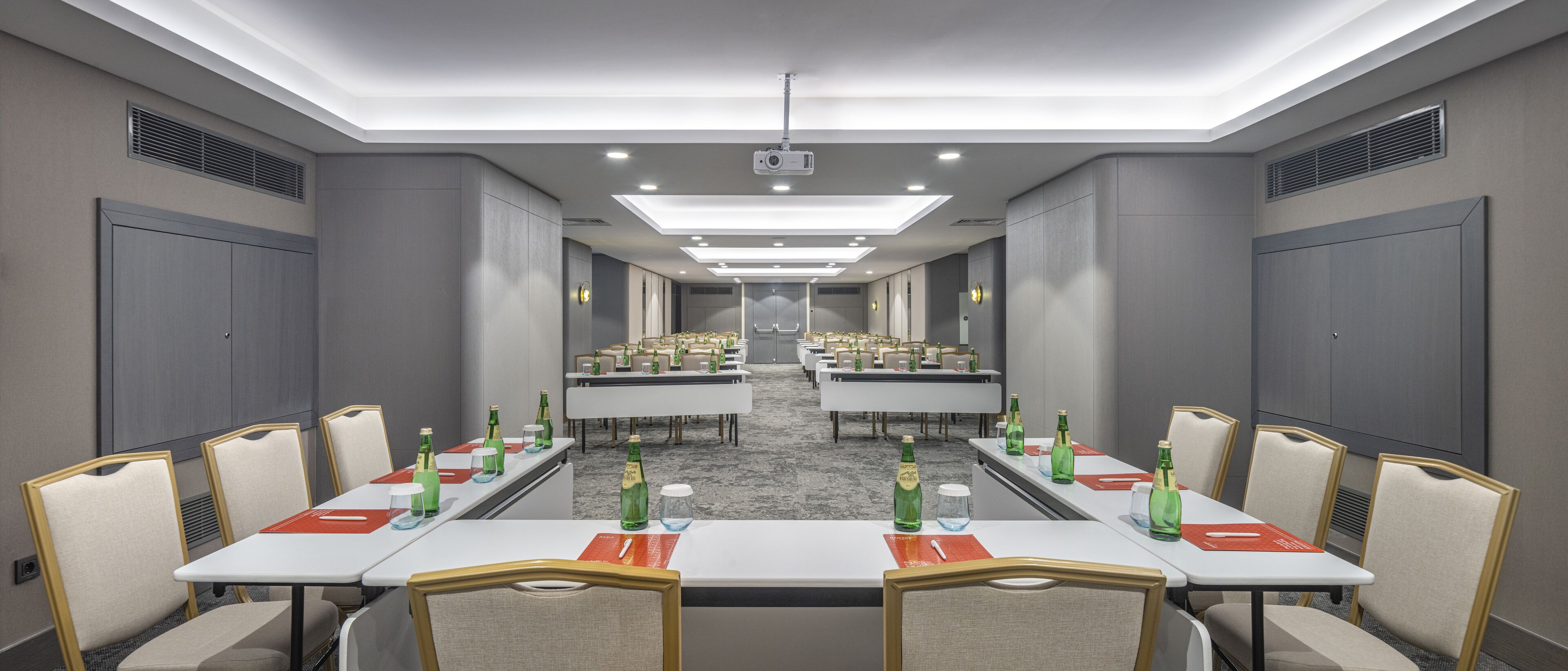 A conference room with multiple tables and chairs, equipped with projectors and lighting.