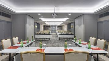A conference room with multiple tables and chairs, equipped with projectors and lighting.