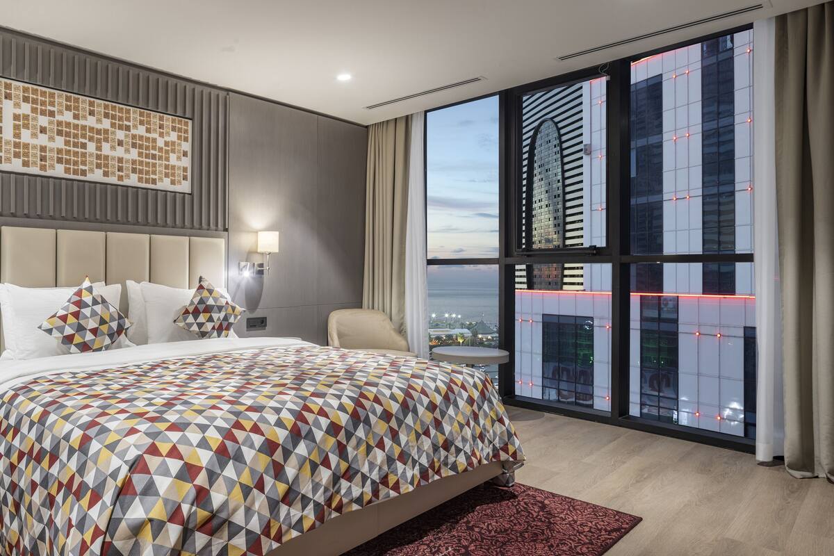 Une chambre d’hôtel moderne avec un grand lit, une vue sur la ville et une couvre-lit à motifs.