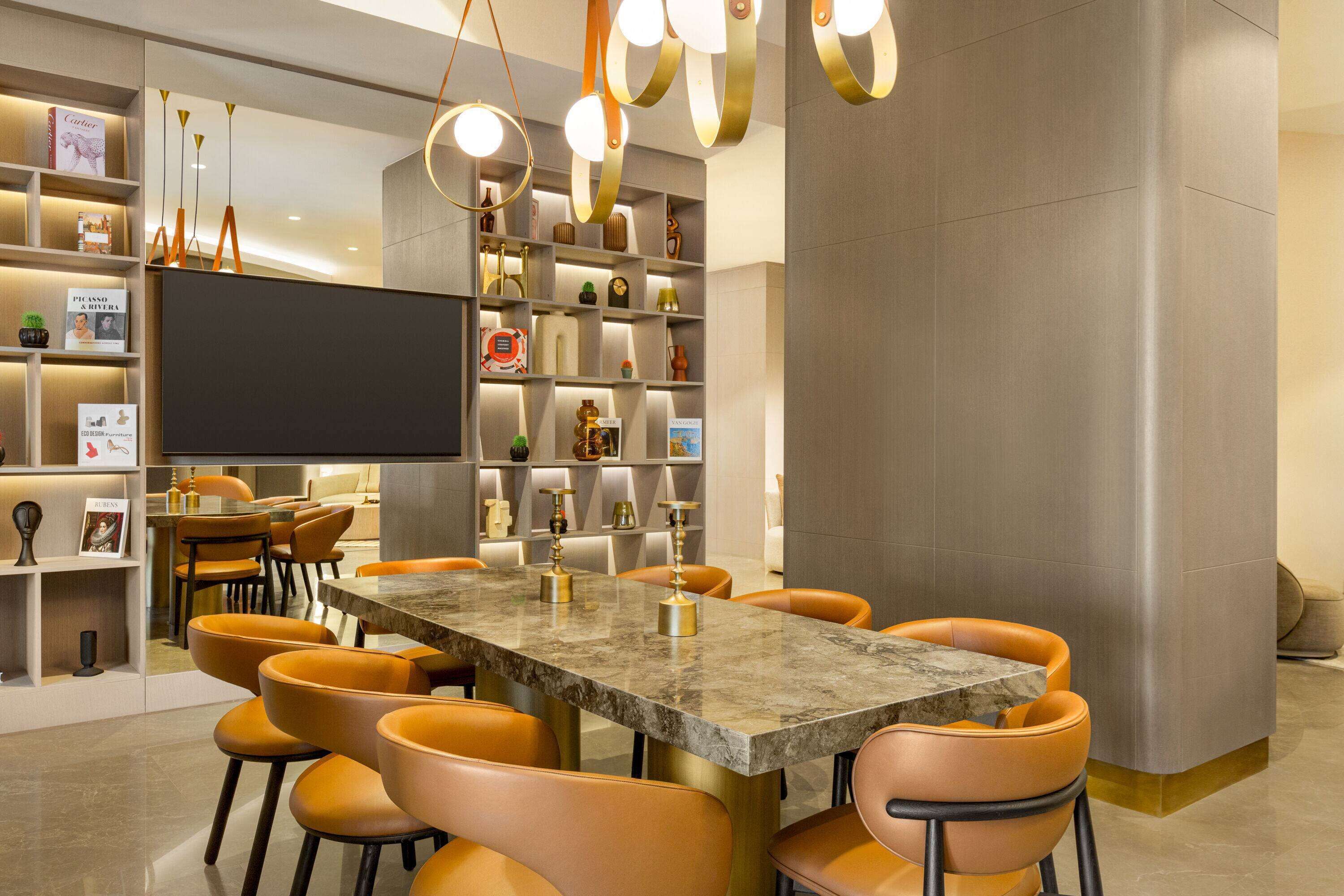 A modern dining area with a marble table, orange chairs, and a bookshelf filled with books and decorative items.
