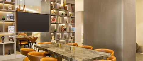 A modern dining area with a marble table, orange chairs, and a bookshelf filled with books and decorative items.