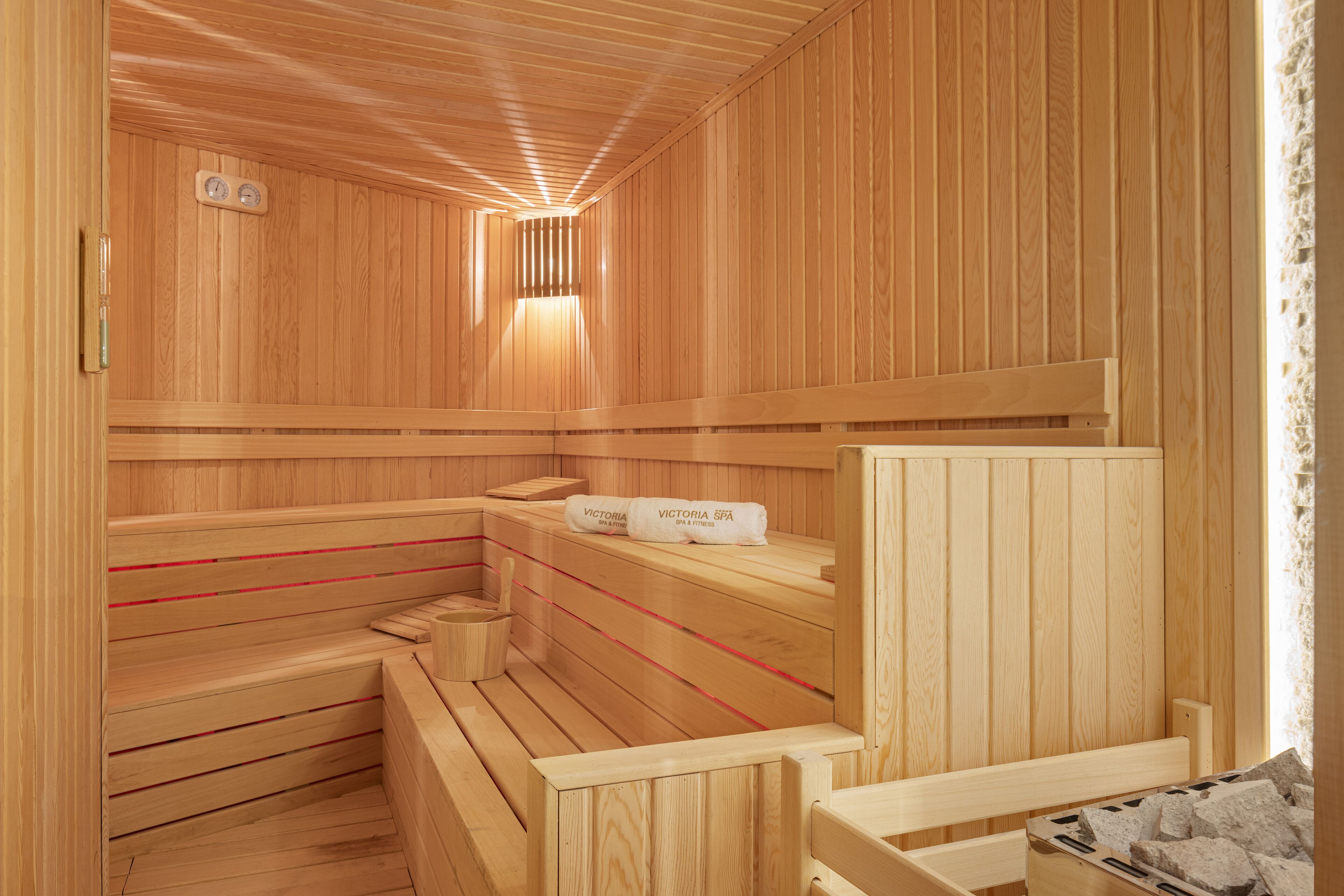 A wooden sauna with benches and a bench seat, a towel rack, and a wall-mounted heater.