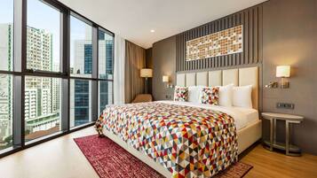 Een moderne hotelkamer met een groot bed, een rood vloerkleed, uitzicht op stadsgebouwen en een wandlamp.