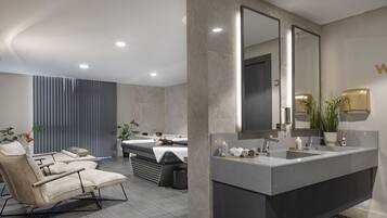 Une salle de bain moderne avec un grand miroir, une baignoire et un coin salon avec un fauteuil.
