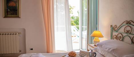 Habitación de hotel con cama, una bandeja de desayuno, ventana con cortinas, radiador y un cuadro en la pared.