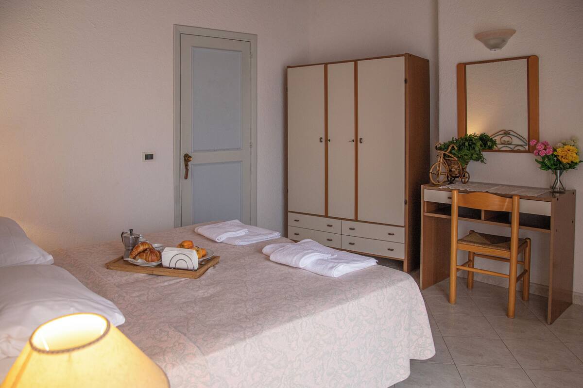 A hotel room with a bed, a wooden desk, a wardrobe, and a tray with breakfast items.