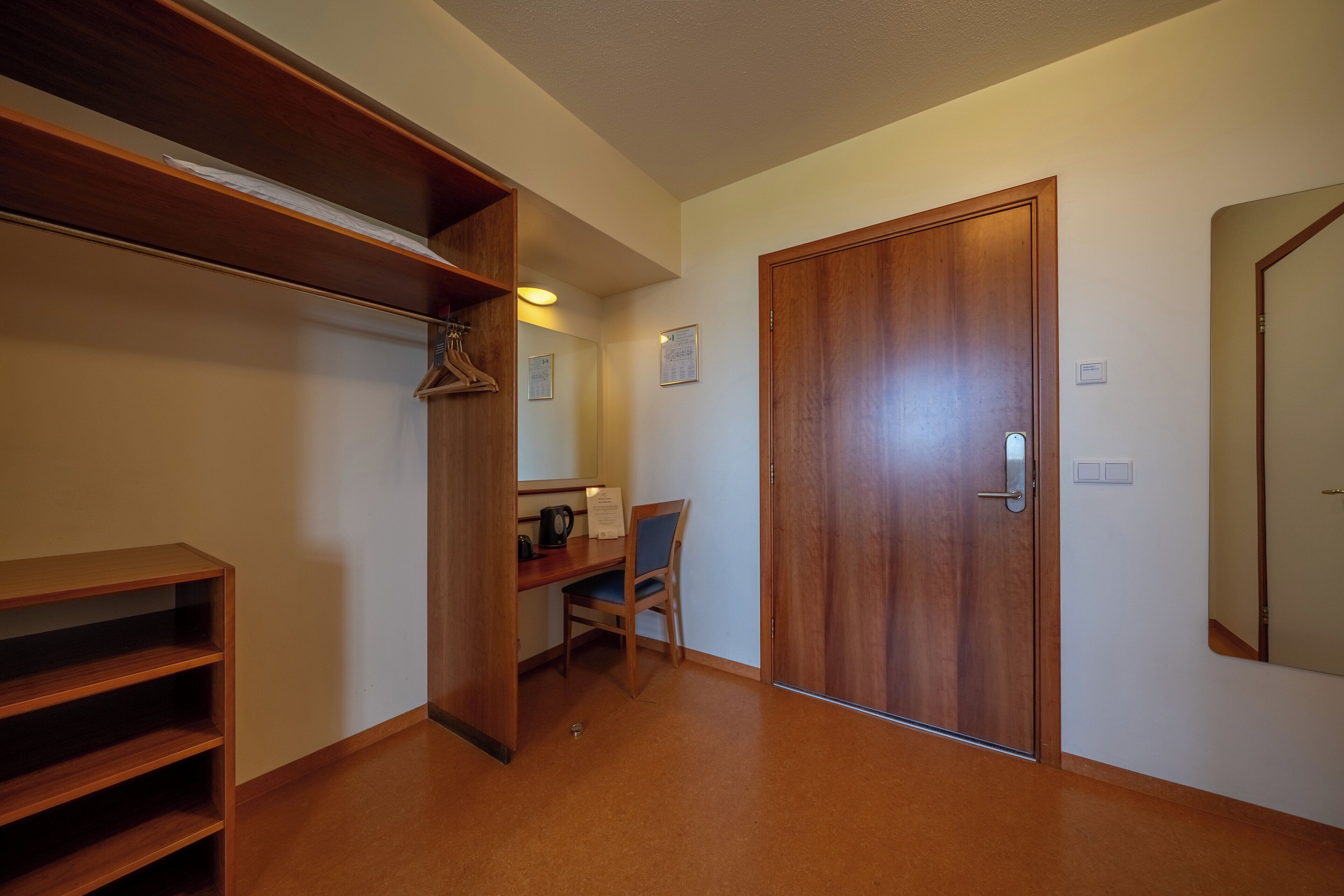 A hallway with a wooden door, a desk with a chair, and a coat rack.