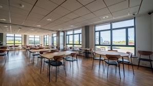 Un amplio espacio interior con varias mesas y sillas, grandes ventanales que ofrecen vistas al exterior y un techo alto con diseños tipo cuadrícula.