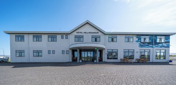 Ett modernt hotell med en central entré, många fönster och sittplatser utomhus.
