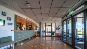 Un hall de hotel con mostrador de recepción, zona de estar y puerta de cristal de entrada.