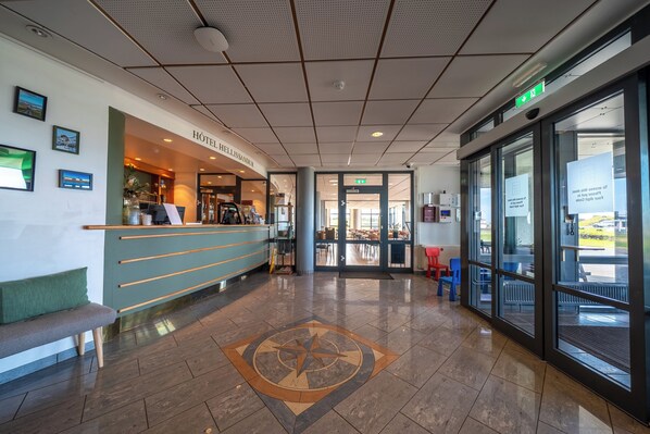 Un hall de hotel con mostrador de recepción, zona de estar y puerta de cristal de entrada.