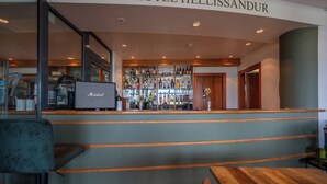 Zona de bar con un letrero que dice "HOTEL HELLISSANDUR" y una variedad de botellas en estantes.