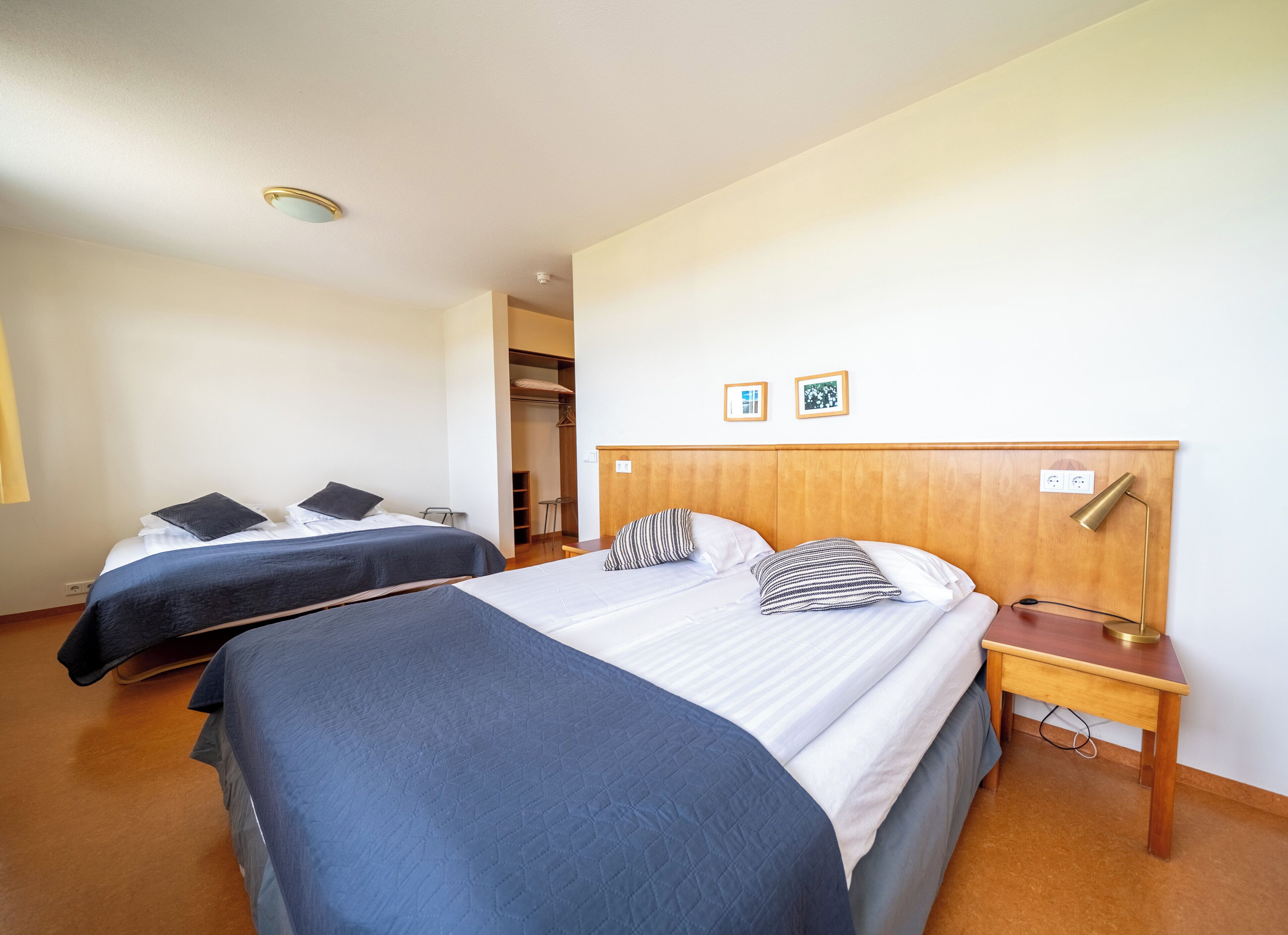 Une chambre d’hôtel avec deux lits, une tête de lit en bois, une table de chevet avec une lampe et une armoire.