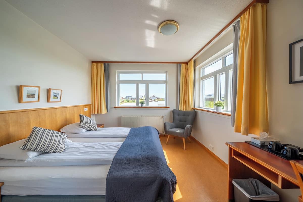 Une chambre d’hôtel avec deux lits, un bureau, une chaise et une fenêtre avec des rideaux.