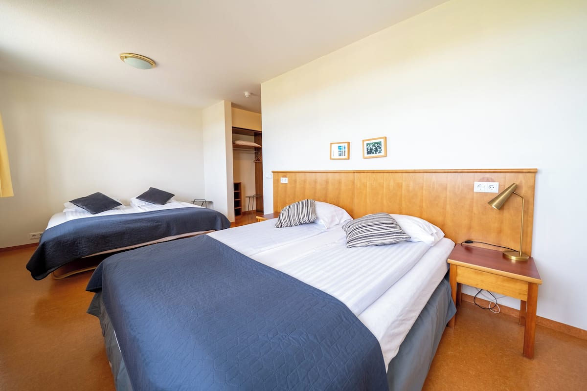Une chambre d’hôtel avec deux lits, une tête de lit en bois, une table de chevet avec une lampe et une armoire.