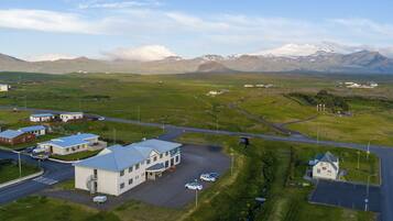 A modern building with a parking area, a small road, and a mountainous backdrop.