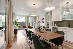 A modern kitchen with white cabinets, a wooden dining table, and pendant lighting. - Spacious Mid-Century Oasis | Heated Pool (New Orleans)