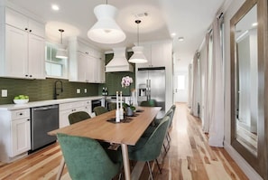 A modern kitchen with white cabinets, a wooden dining table, and green chairs. - Spacious Mid-Century Oasis | Heated Pool (New Orleans)