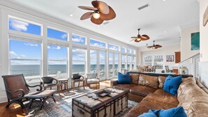 A spacious living room with a large window overlooking the ocean, furnished with leather sofas, chairs, and a coffee table.
