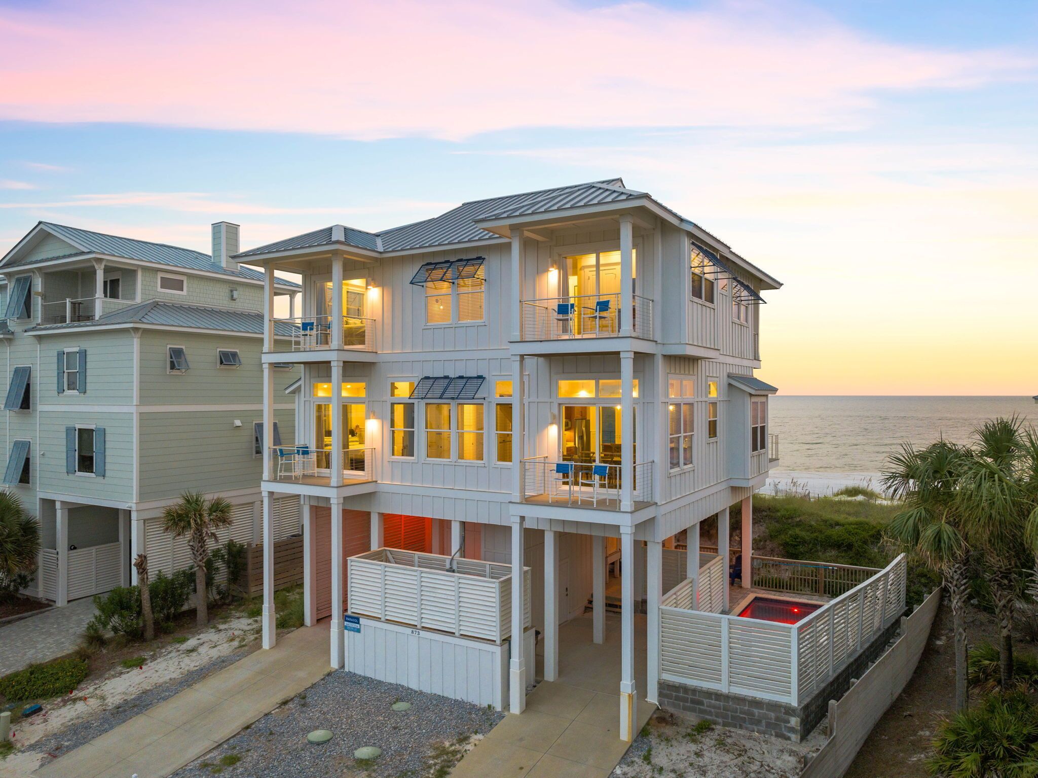 A multi-story beachfront house with balconies, a pool, and a view of the ocean.