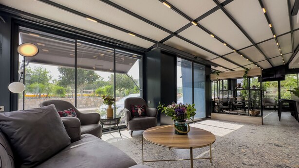 Een moderne lounge met een bank, fauteuils, een ronde salontafel en een groot raam met uitzicht op het omliggende landschap.