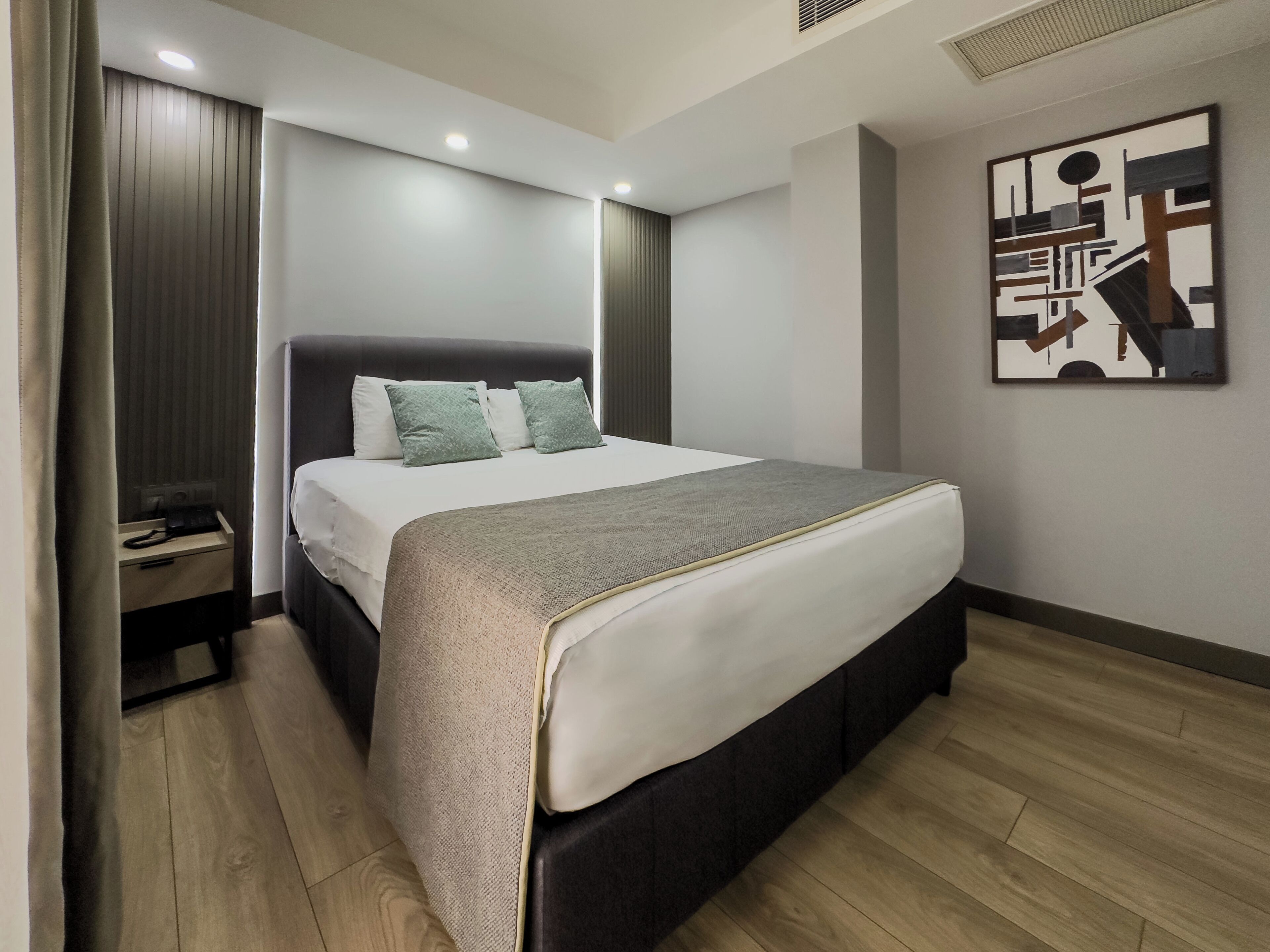 A modern hotel room with a large bed, a bedside table, and a wall-mounted artwork.