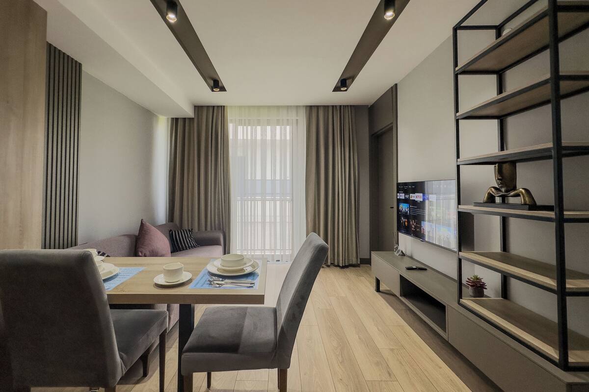Een moderne woonkamer met een eethoek, een bank, een televisie en een boekenkast.