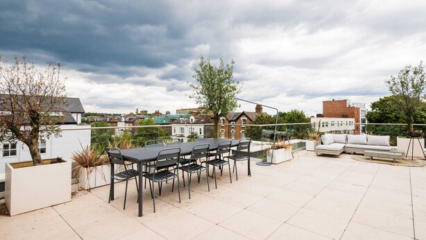 Eine Dachterrasse mit Esstisch und Stühlen, einer Couch und Blick auf die Stadtlandschaft.