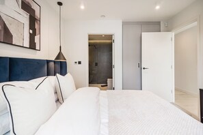 Ein modernes Schlafzimmer mit einem großen Bett, einem Kopfteil, einem Nachttisch, einer Pendelleuchte und einer Tür zu einem Badezimmer.