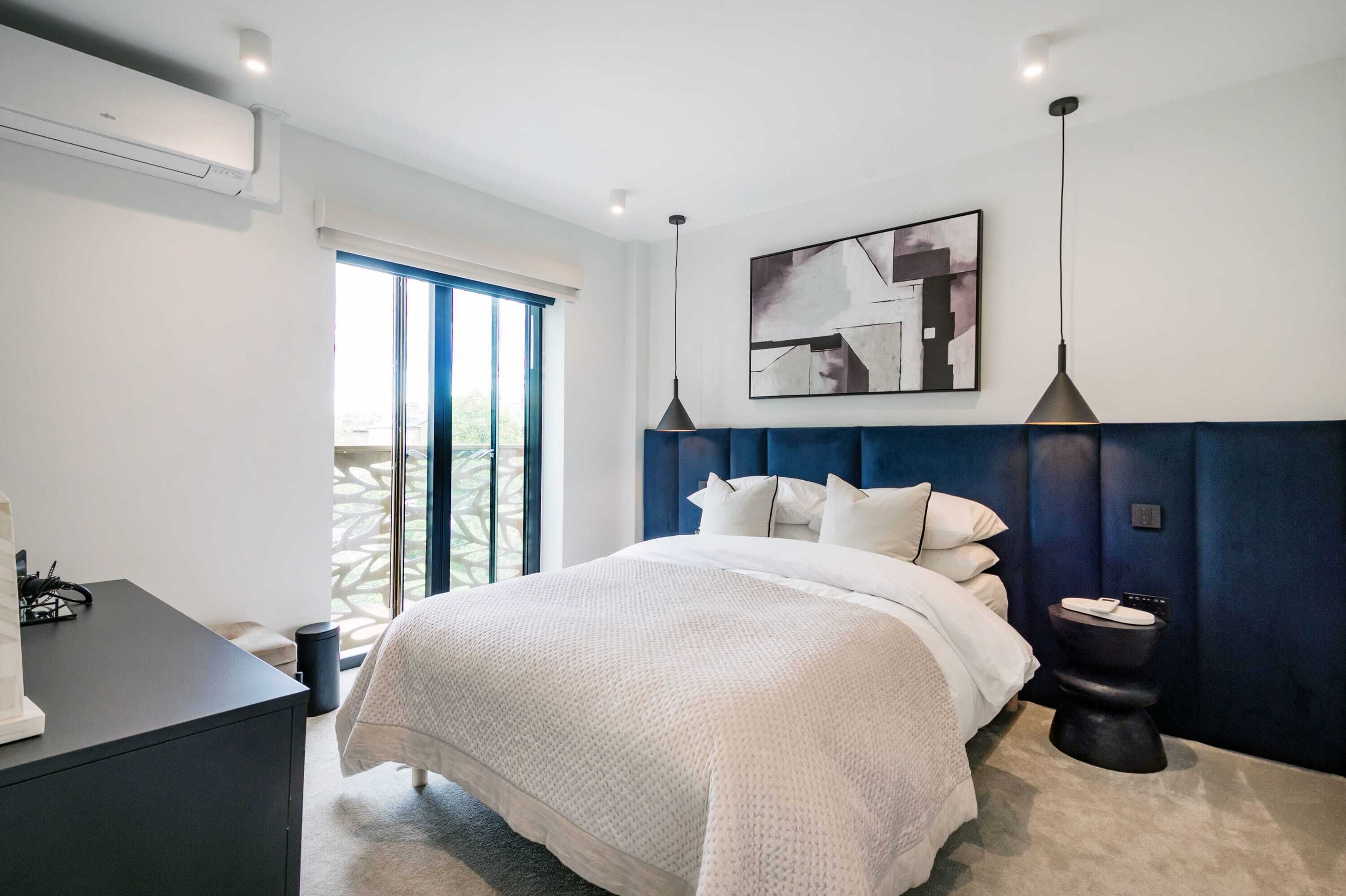 A modern bedroom with a large bed, a desk, and a view of the outdoors.