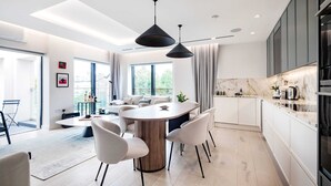 Eine moderne Küche mit Marmorarbeitsplatte, ein Essbereich mit rundem Tisch und Stühlen sowie ein großes Fenster, das für natürliches Licht sorgt.