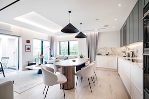 Eine moderne Küche mit Marmorarbeitsplatte, ein Essbereich mit rundem Tisch und Stühlen sowie ein großes Fenster, das für natürliches Licht sorgt.