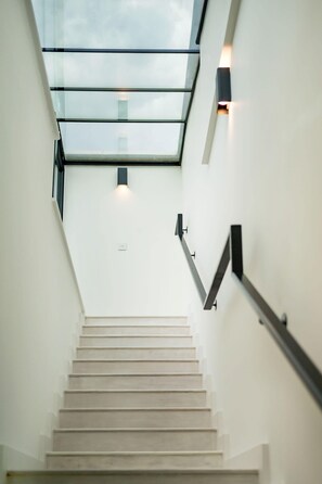 A modern staircase with a glass skylight and wall-mounted lighting fixtures.
