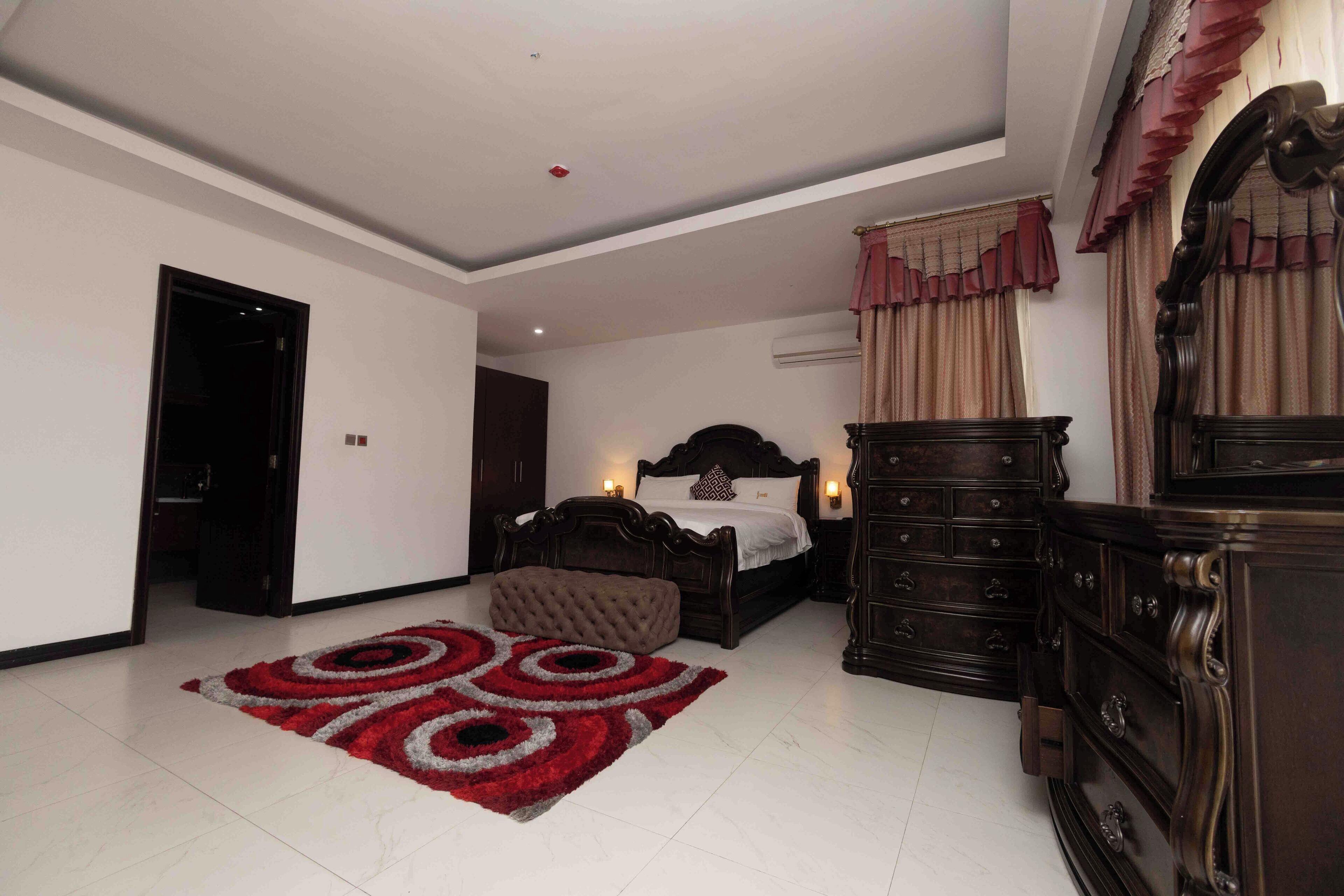 Un dormitorio con cama, cómoda, espejo y alfombra roja.