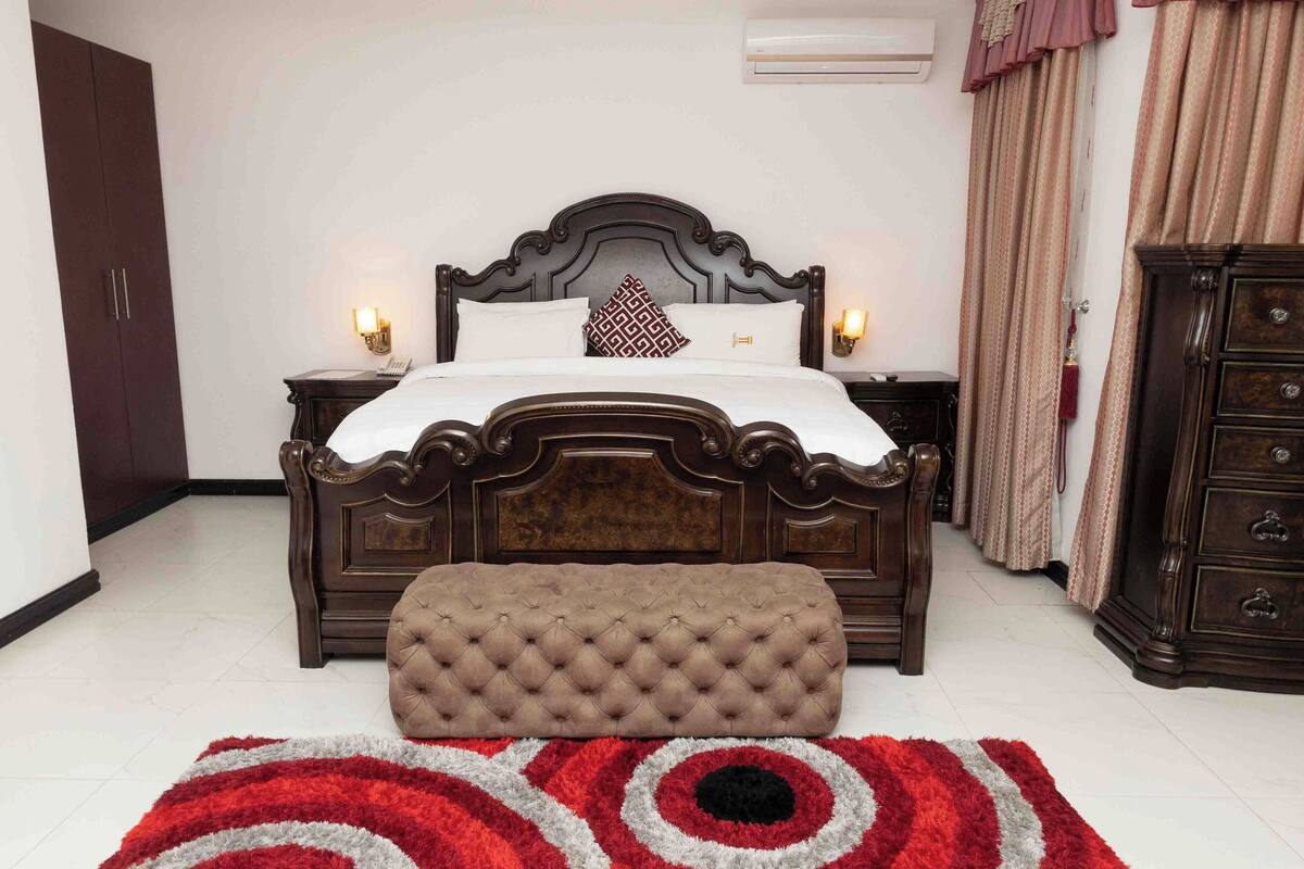 A bedroom with a large bed, a nightstand, a dresser, and a red and white striped rug.