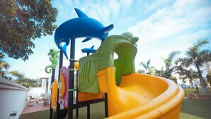 Um parquinho com um escorrega amarelo e diversas estruturas coloridas, incluindo um tubarão azul e criaturas marinhas verdes.