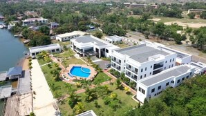 Um hotel moderno com piscina, rodeado por vegetação exuberante e um corpo d'água.