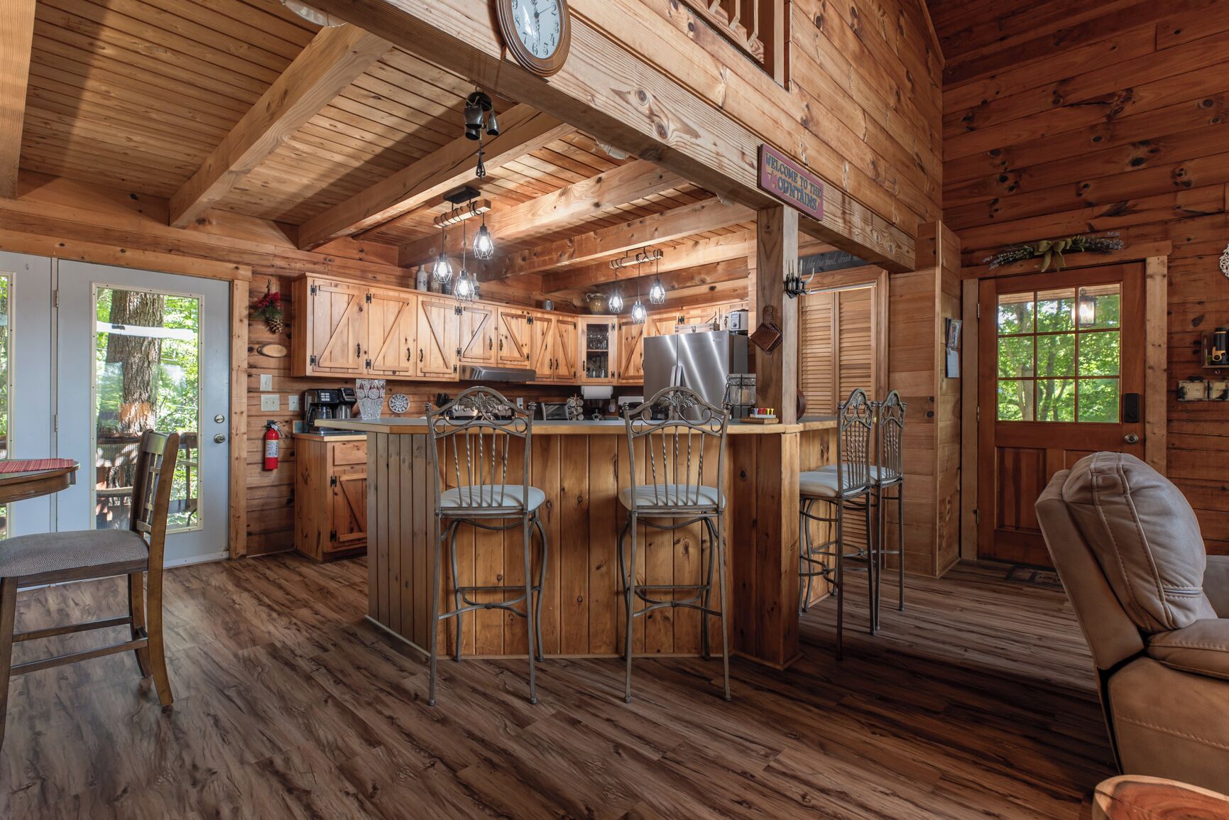 A rustic cabin interior with a wooden bar, bar stools, a dining table, and a cozy seating area.