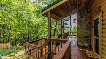 A wooden deck with a stone wall and a wooden door, surrounded by lush greenery.