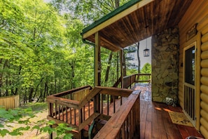 Une terrasse en bois, avec un mur en pierre et une porte en bois, le tout entouré d’une végétation luxuriante.