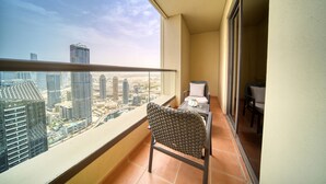 A balcony with a view of a cityscape, a chair, and a table with a lamp.