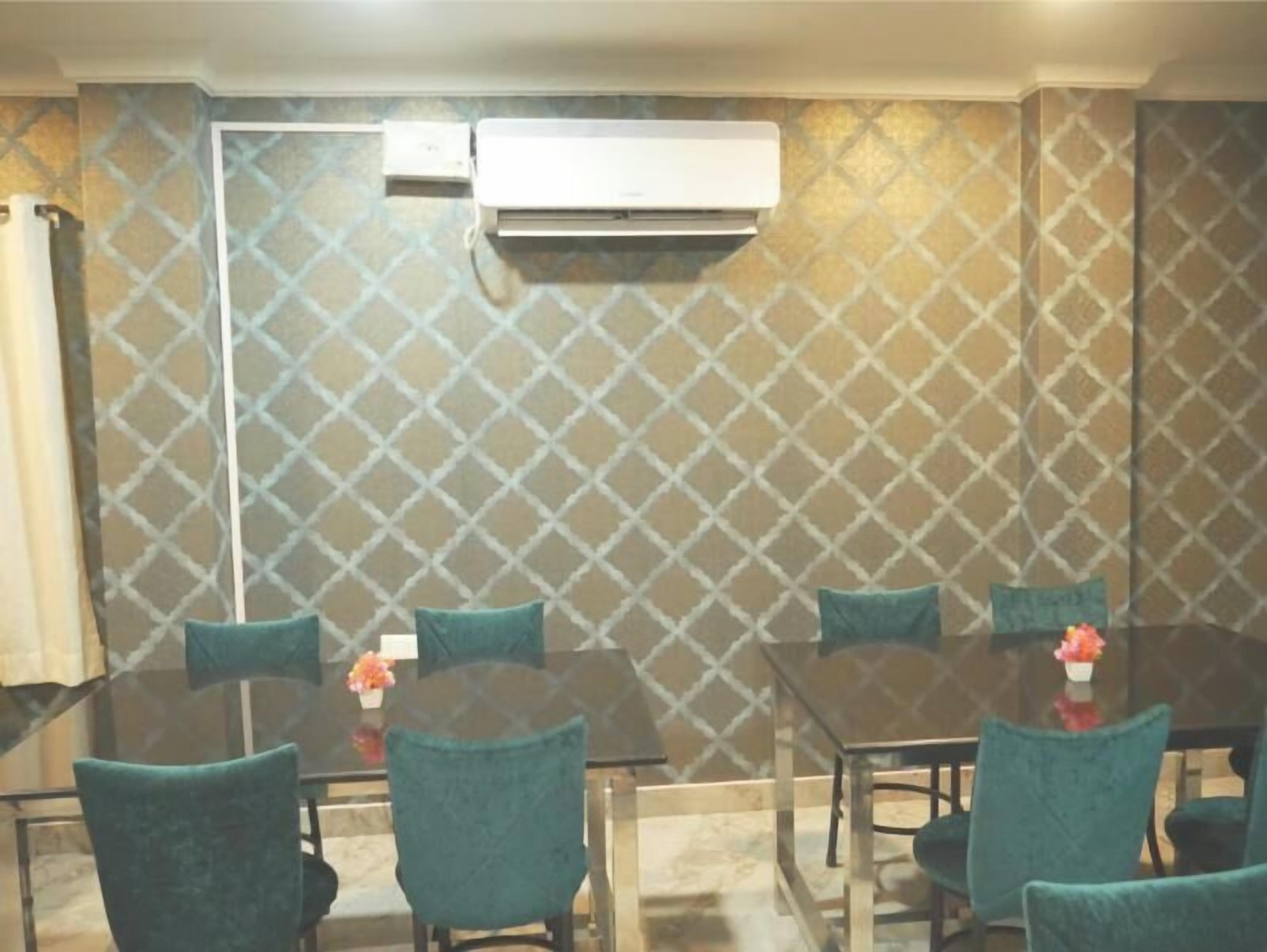 A dining area with a glass table, teal chairs, and a patterned wall.