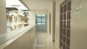 A corridor with a tiled floor, a window, and a door with a grid pattern. - Hotel Pigeons Nest (Port Blair)