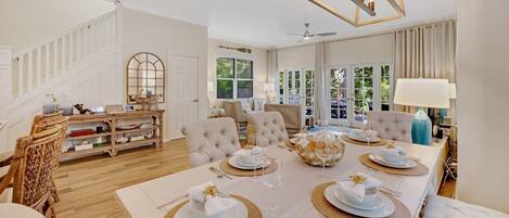 A spacious dining area with a high ceiling, a staircase, and a view of greenery outside.