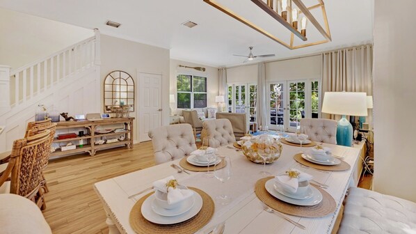 A spacious dining area with a high ceiling, a staircase, and a view of greenery outside.