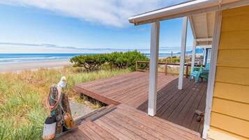 A wooden deck with a covered area, overlooking a beach with a clear sky.