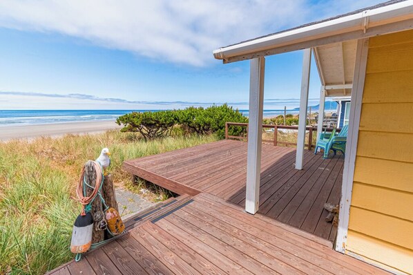 Une terrasse en bois dotée d’un espace abrité, offrant une vue sur une plage sous un ciel dégagé.