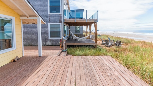 Una casa moderna frente a la playa con una terraza de madera, una hamaca y sillas.