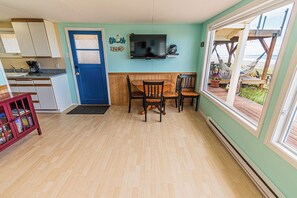 Une pièce chaleureuse avec une table et des chaises en bois, un téléviseur fixé au mur et une vue sur la plage par une grande fenêtre.