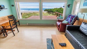 Un salón con un banco de madera, un sofá rojo y una mesa de centro. Hay dos ventanas grandes que ofrecen vistas a la playa y al océano.